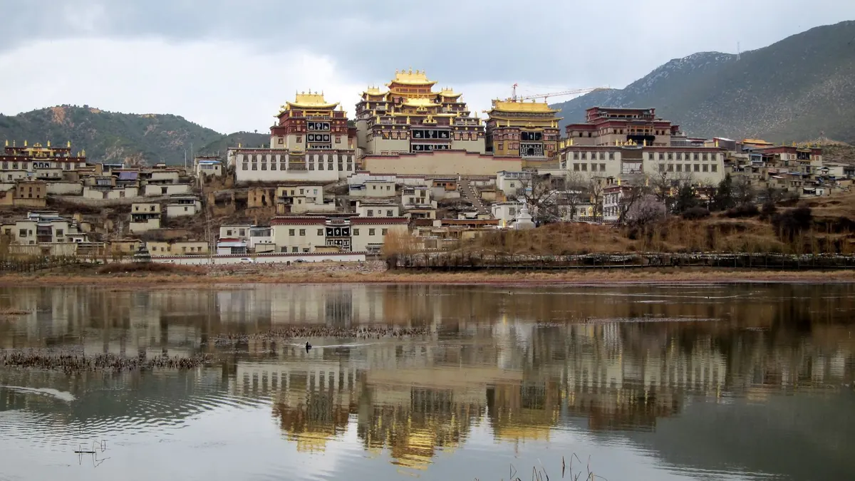 Songzanlin Monastery reflected in a calm lake under highland mountains in Shangri-La